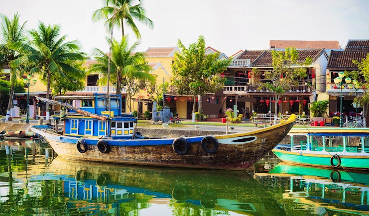 Wooden boat moored up Thu Bon River in Hoi An, riverside houses, palm trees