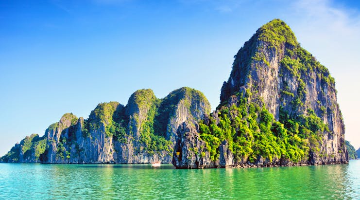 Ha Long Bay rock formation in sea, tall rocks covered in greenery