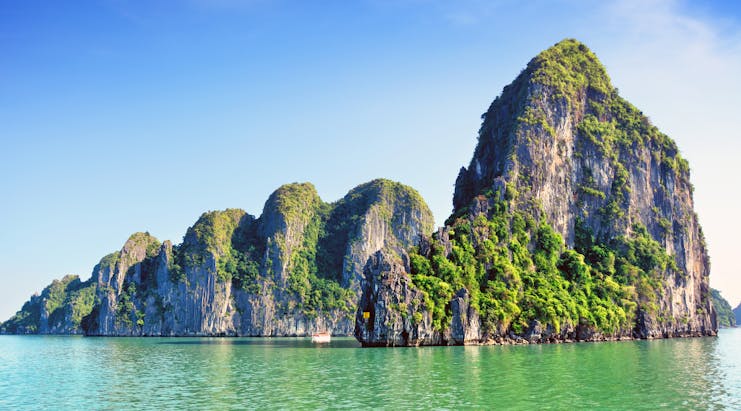 Ha Long Bay rock formation in sea, tall rocks covered in greenery