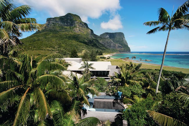 Capella Lodge exterior, modern architexture, exterior seating area, lush greenery, beach and mountains in background