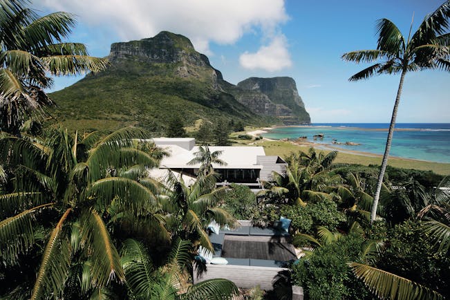Capella Lodge exterior, modern architexture, exterior seating area, lush greenery, beach and mountains in background
