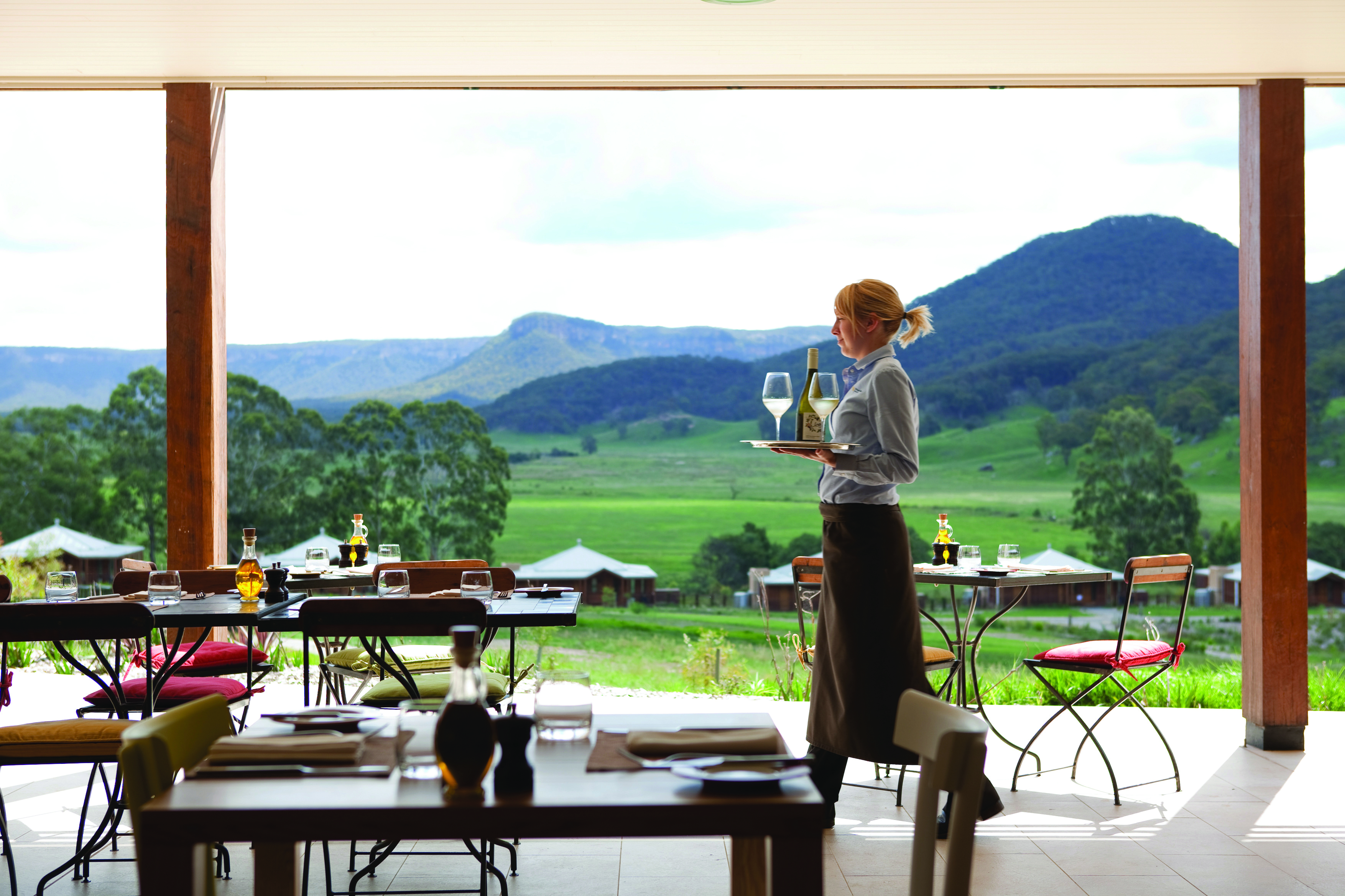 Dining area with tables set up outside with a veranda over the top, looking out over mountains 
