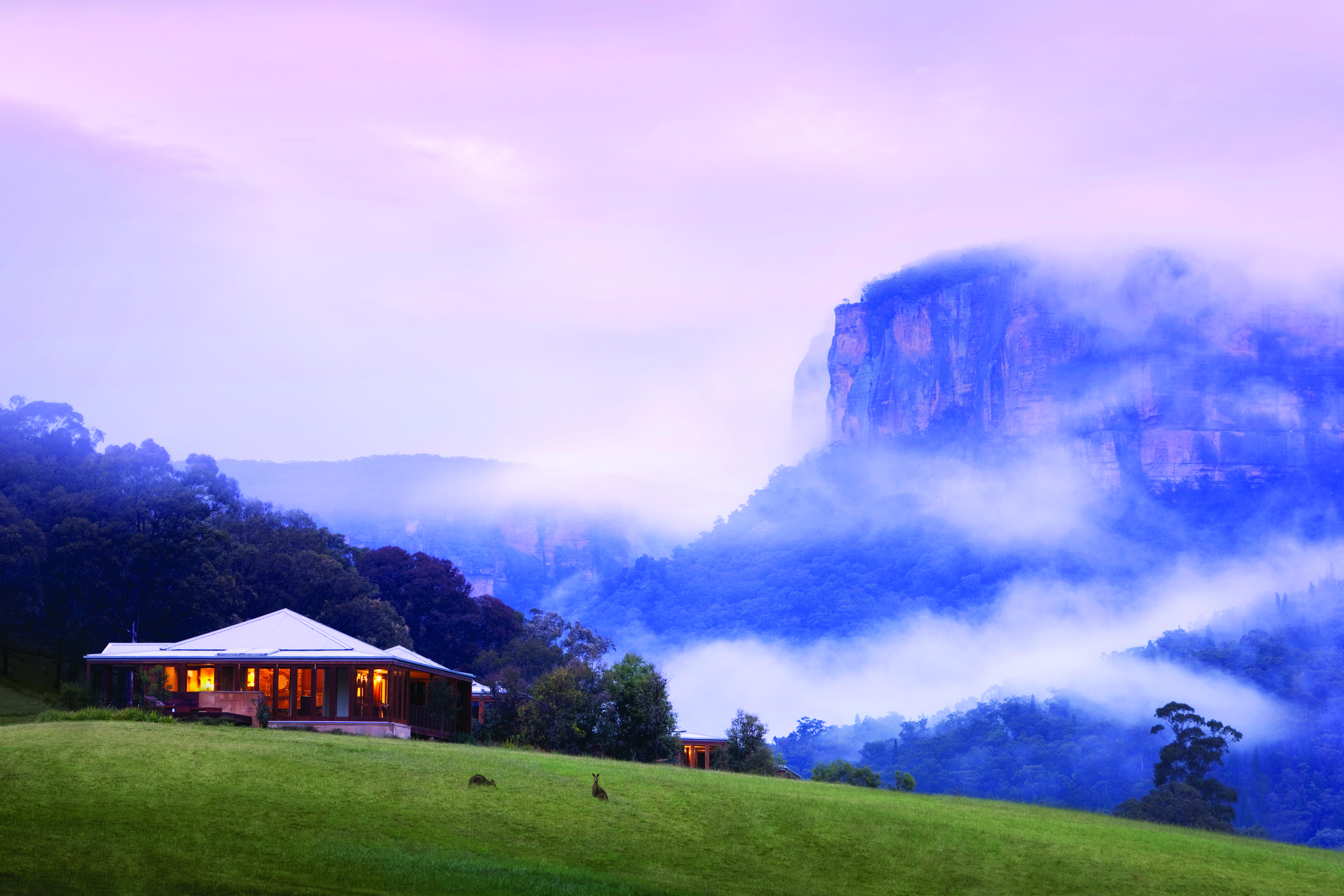 Exterior of the hotel in mist shown with clouds around it and mountains beside 
