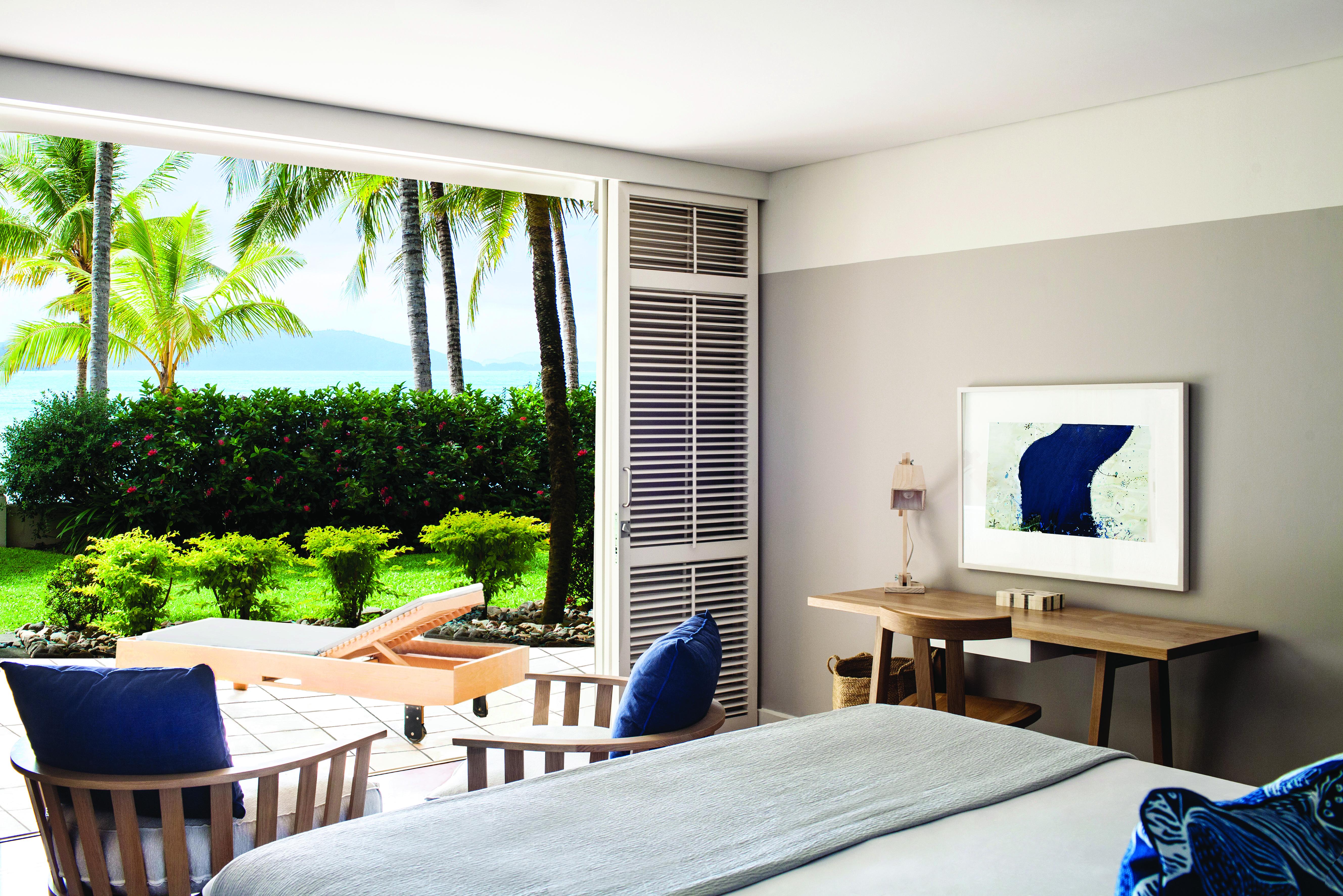 Beach Club Hamilton guestroom, double bed, modern decor, doors leading to terrace with sun loungers, overlooking the sea