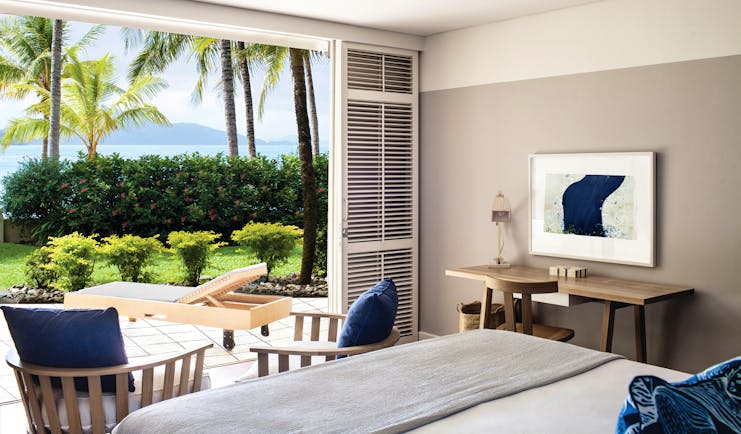 Beach Club Hamilton guestroom, double bed, modern decor, doors leading to terrace with sun loungers, overlooking the sea