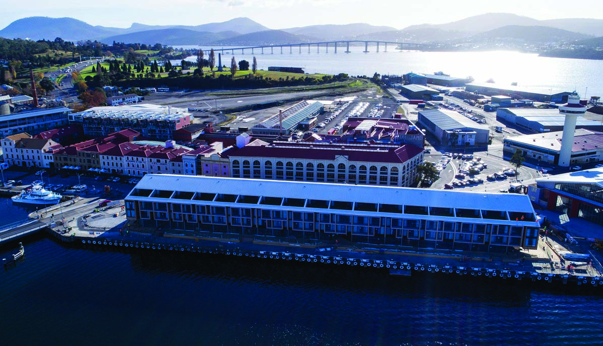 MACq01 exterior, hotel building on edge of marina, buildings in the background, mountains on the horizon