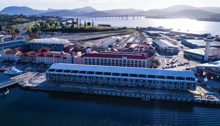 MACq01 exterior, hotel building on edge of marina, buildings in the background, mountains on the horizon