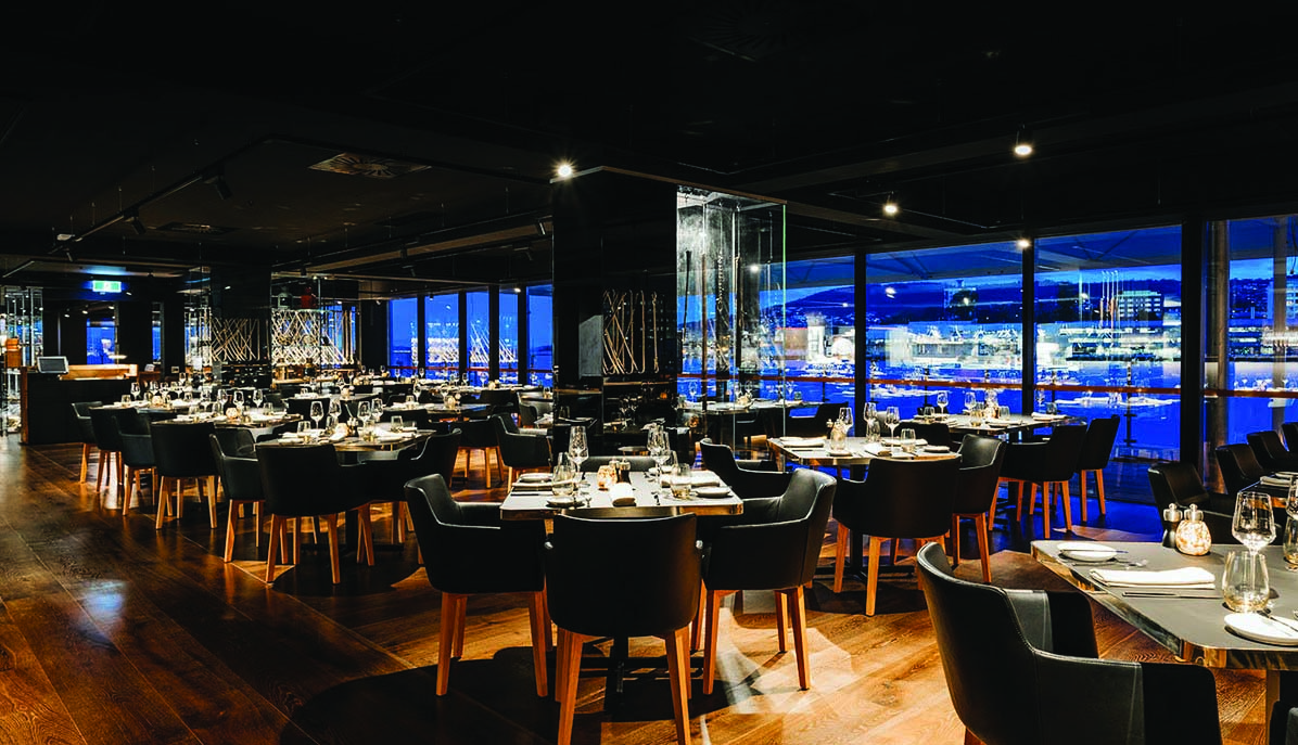 MACq01 restaurant, indoor dining area, tables and chairs with modern decor, large windows with views over the sea