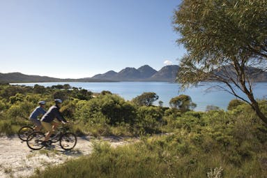 Saffire Freycinet Tasmania nature cycling two people cycling on dirt track with view of mountain and sea