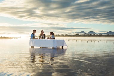 Saffire Freycinet Tasmania outdoor dining people at a table in the water at sunset shucking oysters