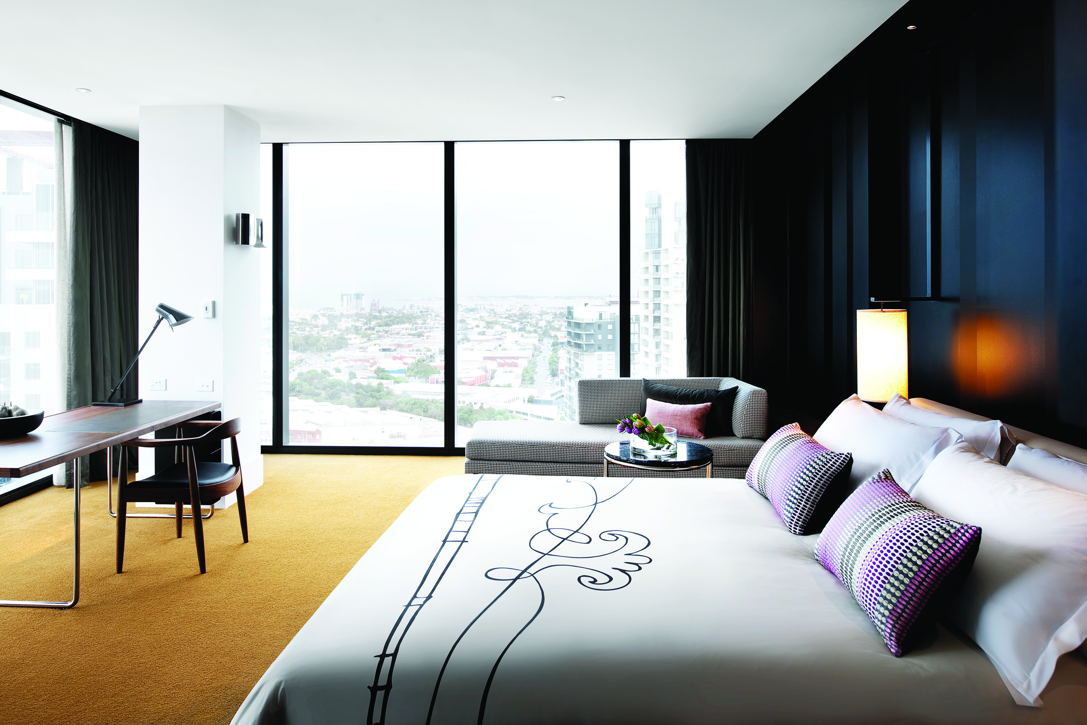 Luxury suite with window pannelled walls looking out over the city, armchairs and a large double bed