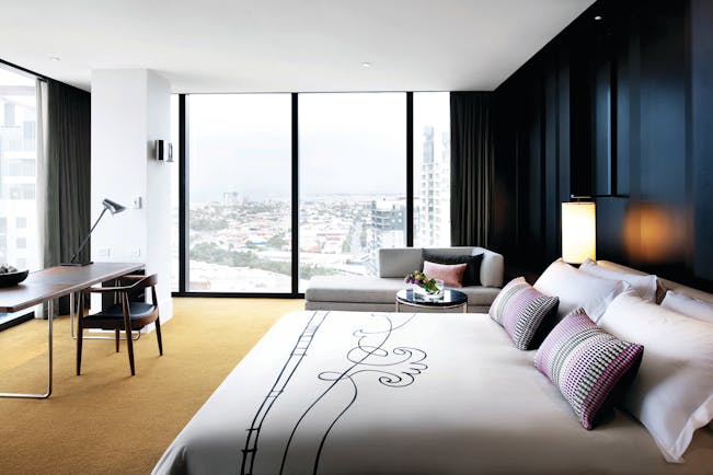 Luxury suite with window pannelled walls looking out over the city, armchairs and a large double bed