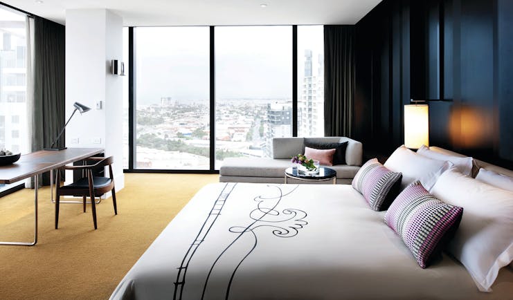 Luxury suite with window pannelled walls looking out over the city, armchairs and a large double bed