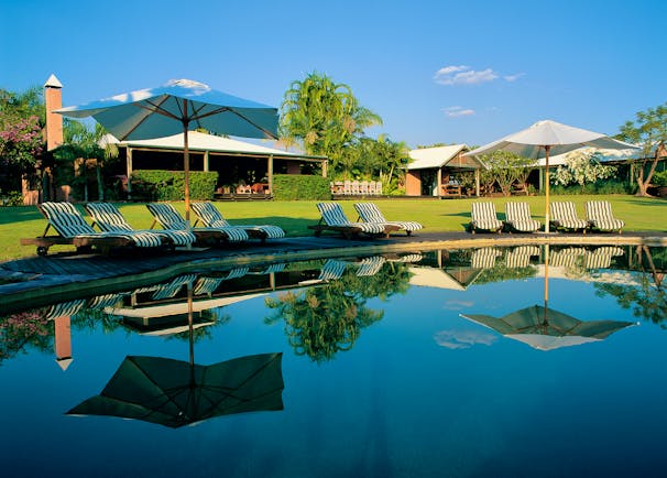 Outdoor pool with sun loungers and umbrellas around the edge, reflecting in the water 