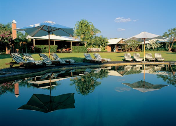 Outdoor pool with sun loungers and umbrellas around the edge, reflecting in the water 