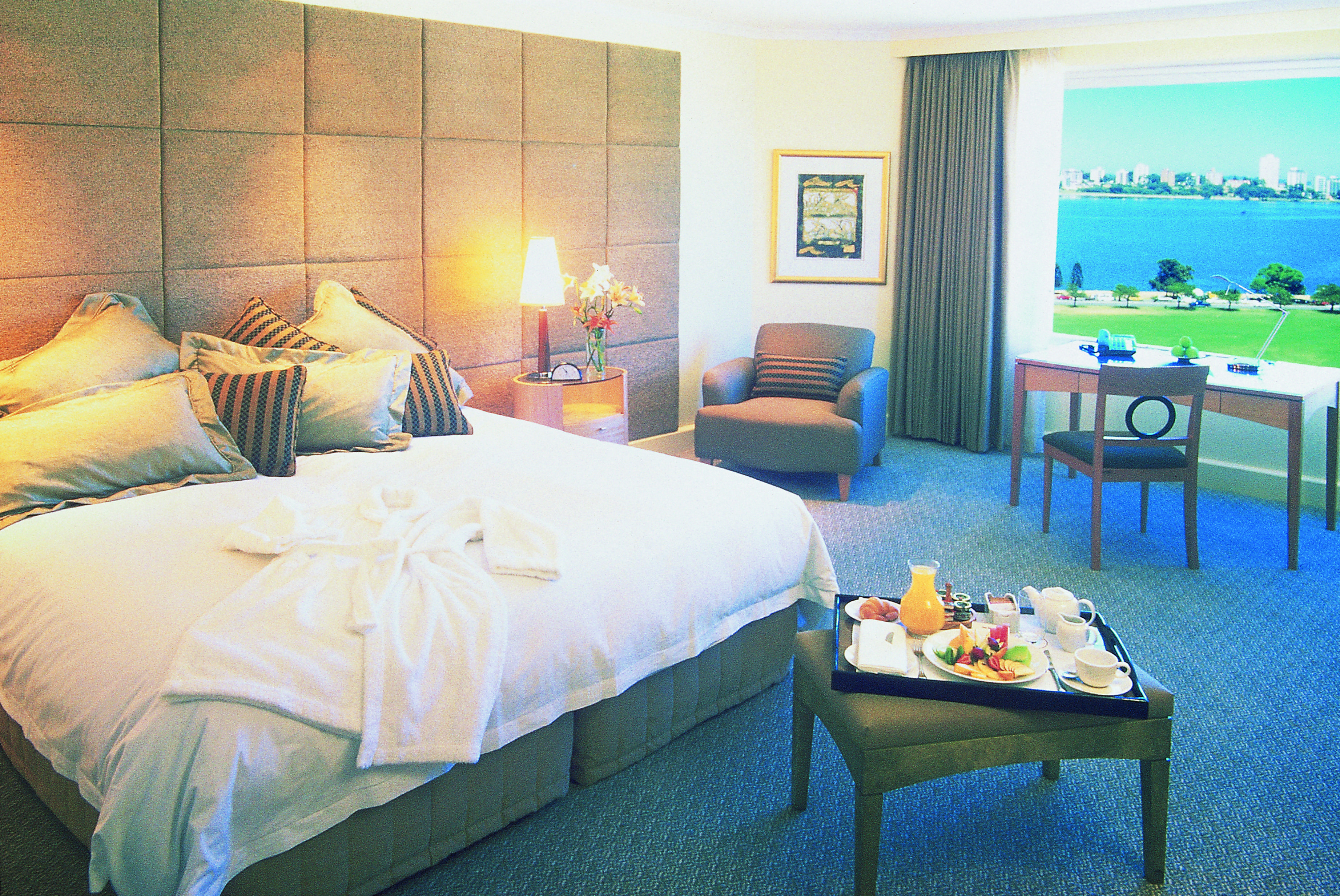 Bedroom with large double bed, arm chair and large window with views over ocean 