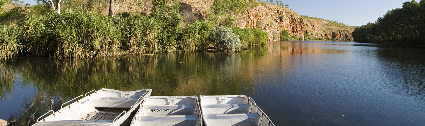 Three open boats on deep blue lake with trees and mountains