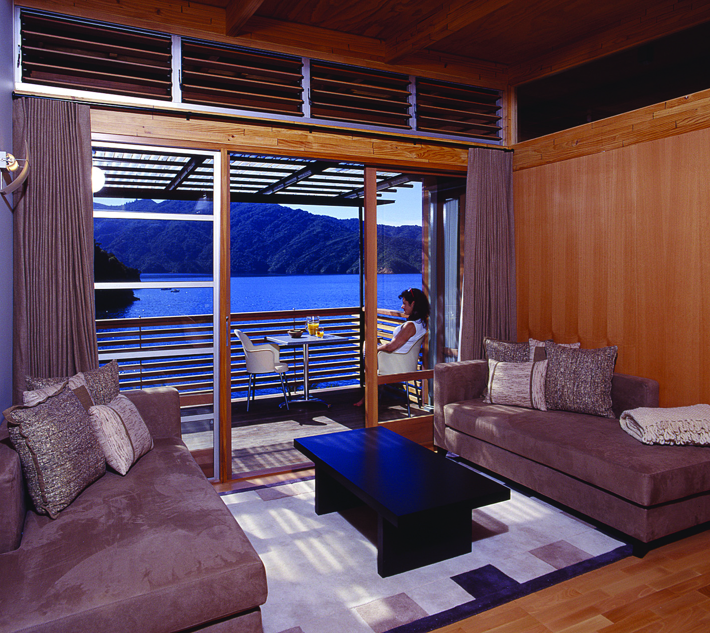 Bay of Many Coves Marlborough and Blenheim lounge area and woman sitting on a balcony with water and mountain view