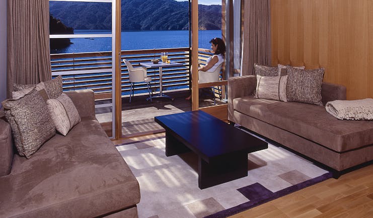 Bay of Many Coves Marlborough and Blenheim lounge area and woman sitting on a balcony with water and mountain view