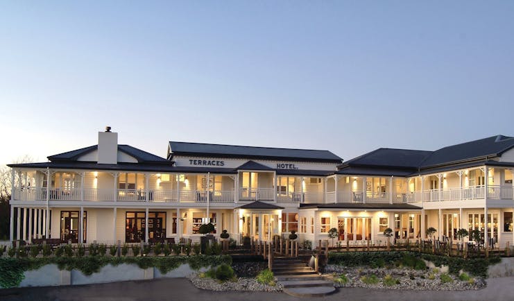 Exterior view of Hilton Lake Taupo with white building, dark tiled roof and lights inside lighting the yellow up with a yellow glow