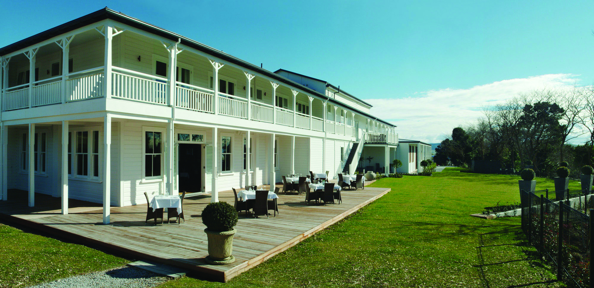 Exterior view of hotel and terrace on bottom floor with seating areas set out near the grass