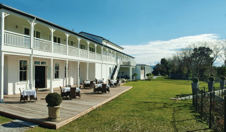 Exterior view of hotel and terrace on bottom floor with seating areas set out near the grass