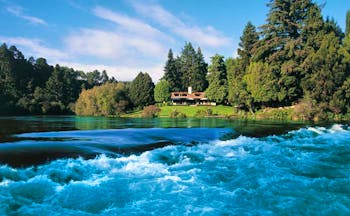 Huka Lodge Central North Island falls aerial view of a lodge and gardens surrounded by trees near river with rapids