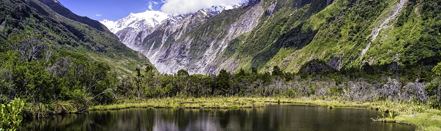 Mountain scene with lake and grey mountains in distance looking at Franz Josef glacier