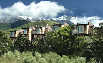 Hapuku Lodge Central South Island exterior wooden chalets on stilts among trees with mountain view