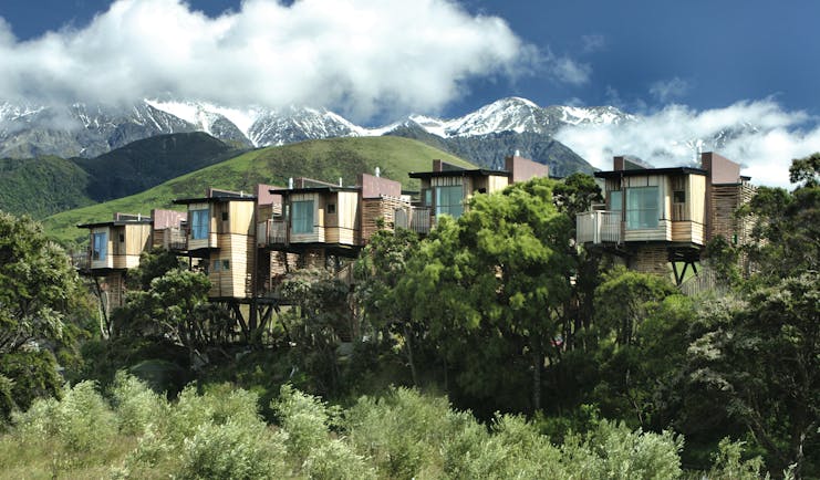 Hapuku Lodge Central South Island exterior wooden chalets on stilts among trees with mountain view
