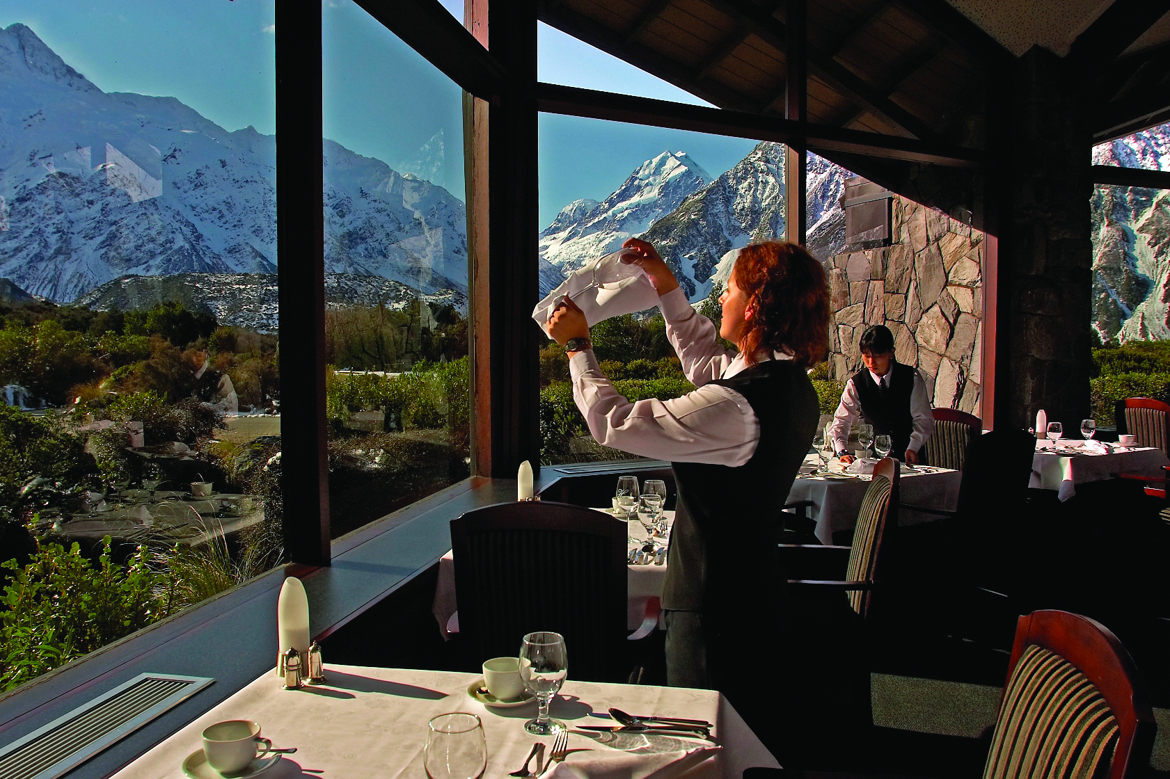The Hermitage Hotel Central South Island restaurant woman cleaning wine glass in dining room with mountain views