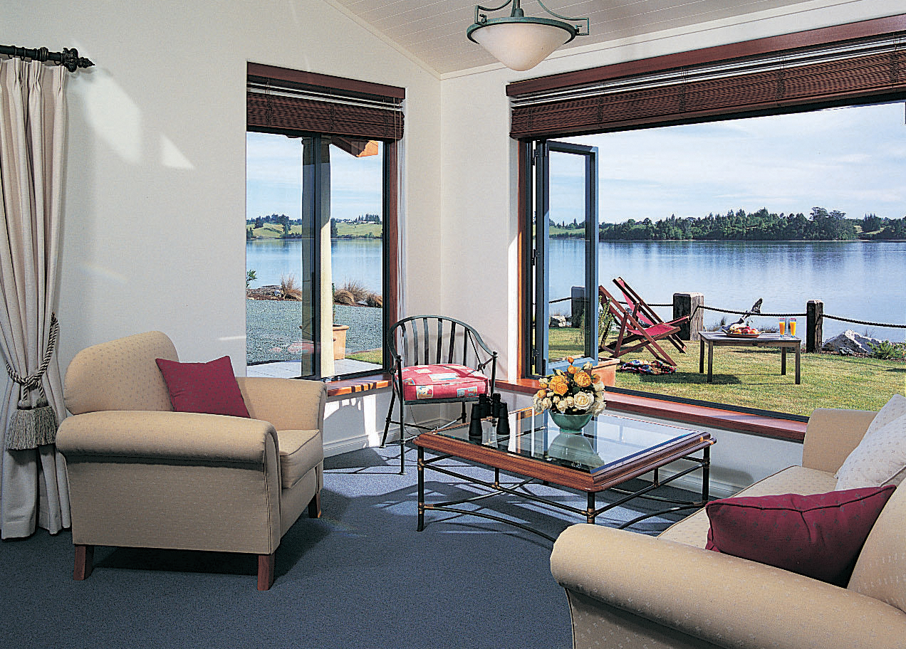 Lounge area with arm chairs and coffee table inside with doors opening onto a terrace overlooking water 