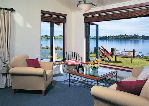 Lounge area with arm chairs and coffee table inside with doors opening onto a terrace overlooking water 