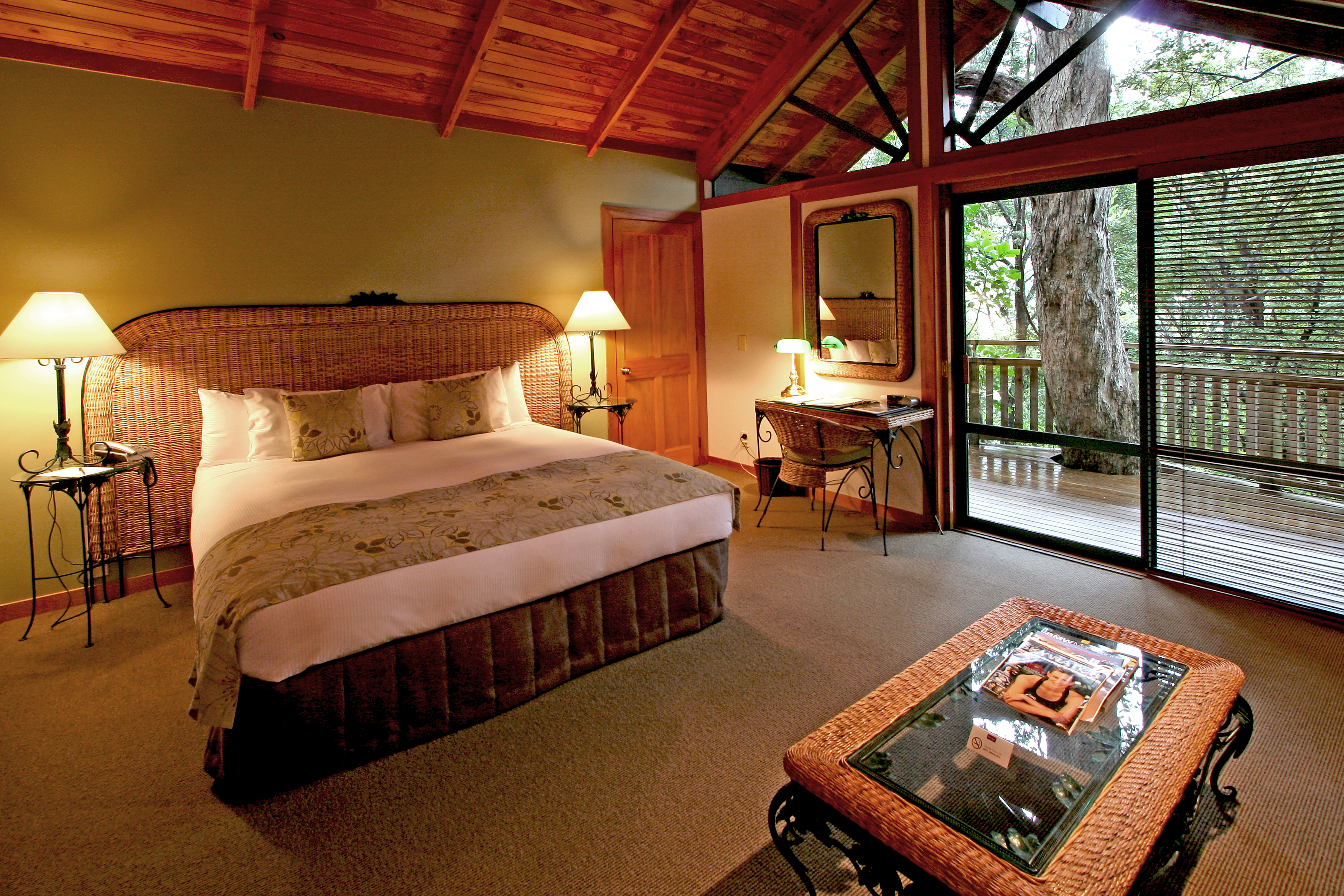 Grand Mercure Puka Park Northlands and Bay of Islands bedroom with wicker head board and balcony with tree