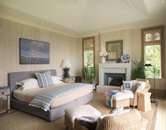 Kauri Cliffs master bedroom, cosy pastel decor, bed, armchairs