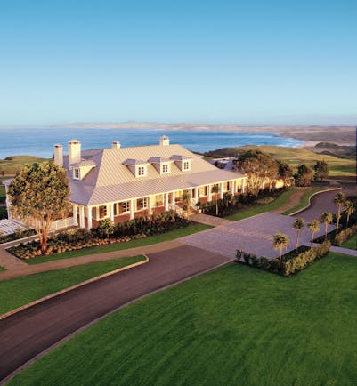 Exterior shot of Kauri Cliffs, hotel building, lawns, sea in backgroubnd