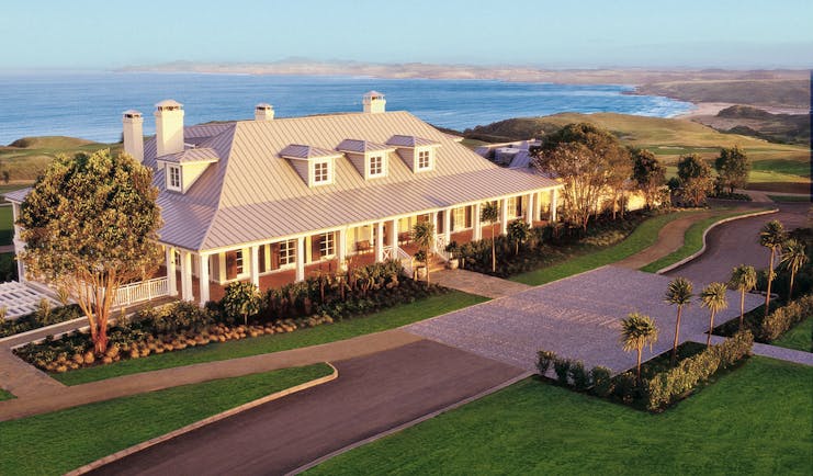 Exterior shot of Kauri Cliffs, hotel building, lawns, sea in backgroubnd
