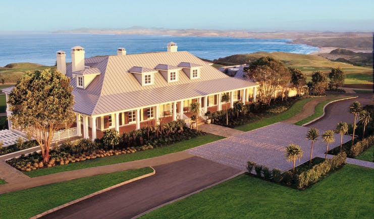 Exterior shot of Kauri Cliffs, hotel building, lawns, sea in backgroubnd
