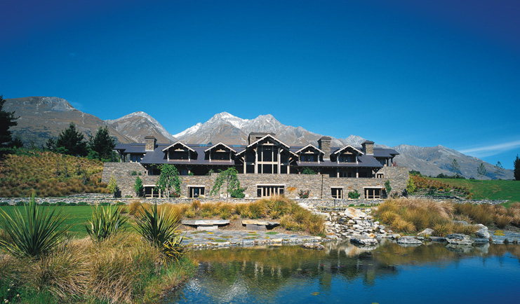 Blanket Bay Otago and Fiordland exterior stone lodge overlooked by snow capped mountain next to lake