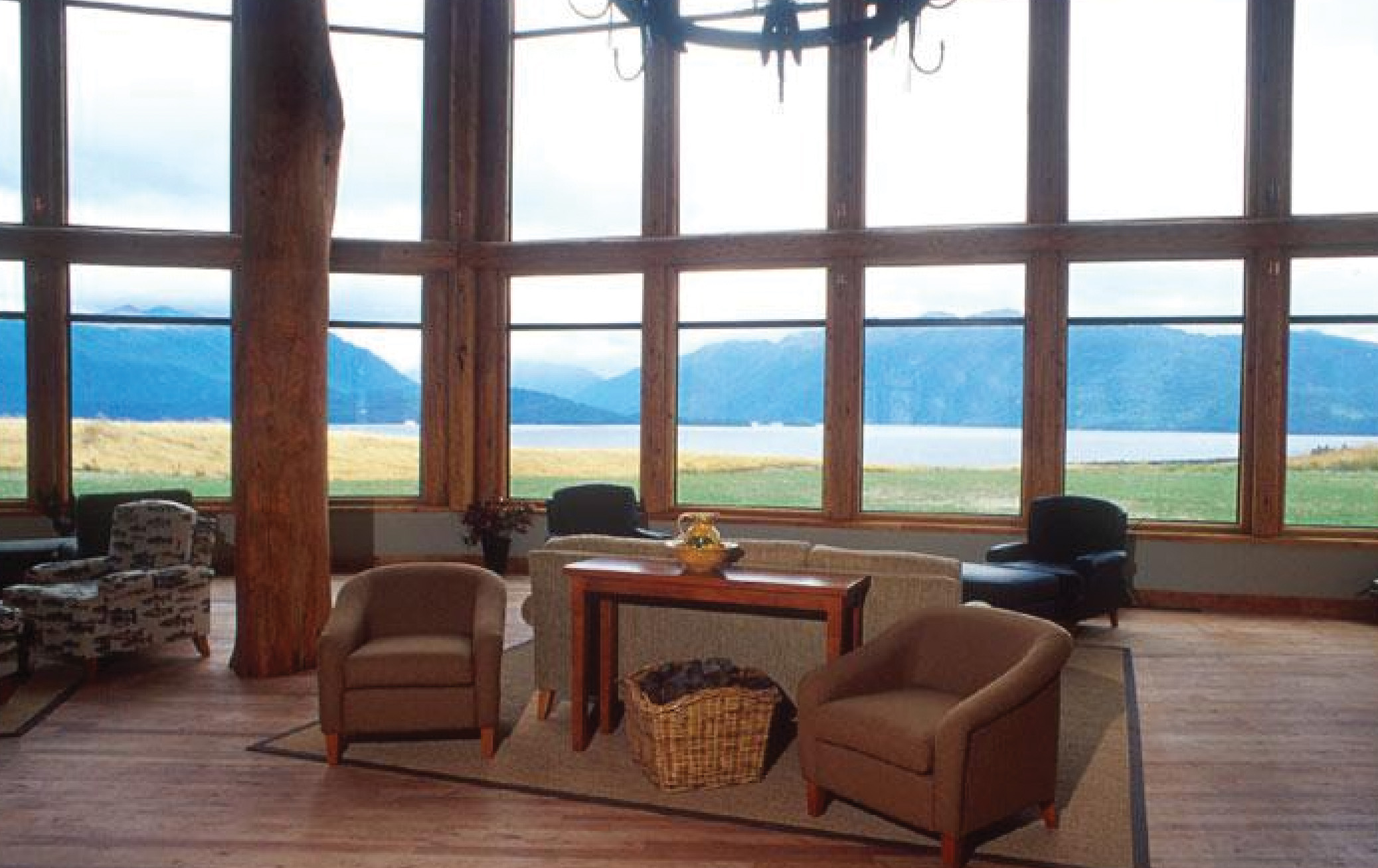 Fiordland Lodge sitting area with wooden floors, armchairs and wood pannelled windows looking over mountains 