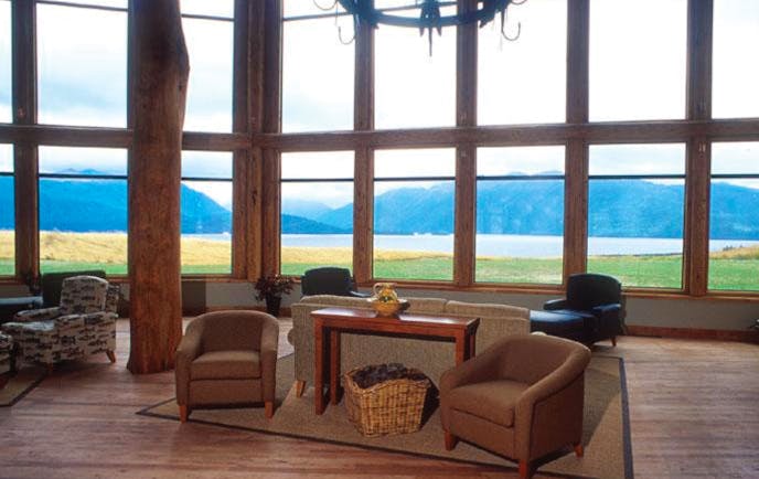 Fiordland Lodge sitting area with wooden floors, armchairs and wood pannelled windows looking over mountains 