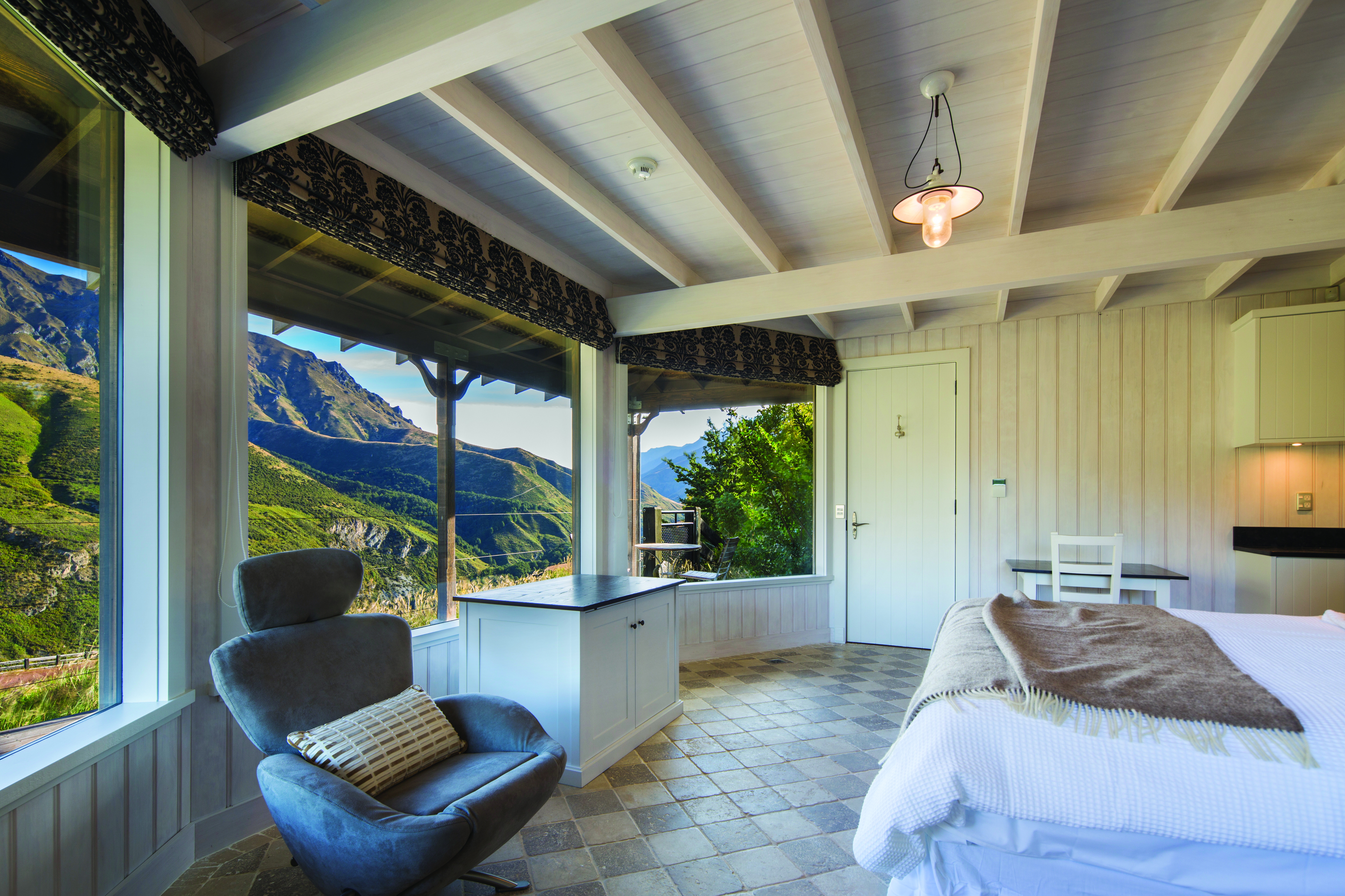 Mahu Whenua Otago and Fiordland cottage bedroom with armchair and panoramic windows with mountain view