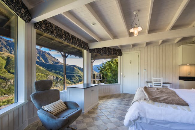 Mahu Whenua Otago and Fiordland cottage bedroom with armchair and panoramic windows with mountain view