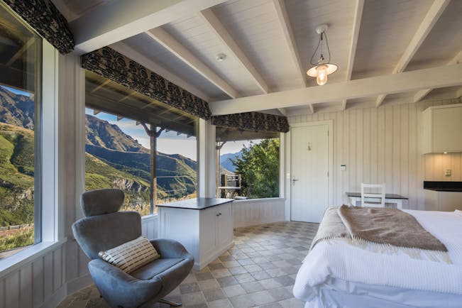 Mahu Whenua Otago and Fiordland cottage bedroom with armchair and panoramic windows with mountain view