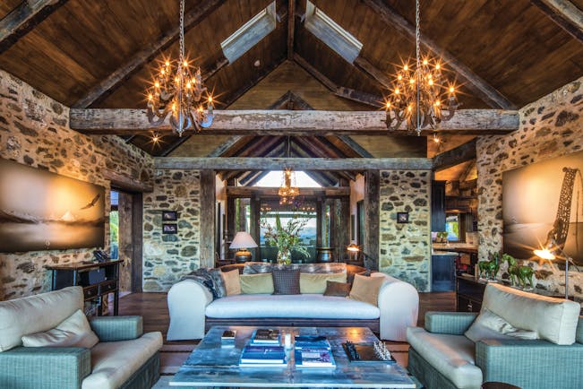 Mahu Whenua Otago and Fiordland living room with exposed stone and beams and chandeliers