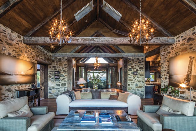 Mahu Whenua Otago and Fiordland living room with exposed stone and beams and chandeliers