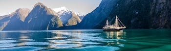 Icy green water with steep grey mountains behind and cruise ship