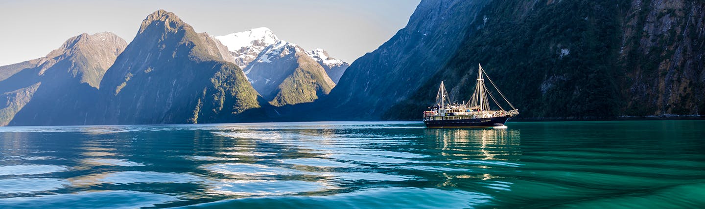 Icy green water with steep grey mountains behind and cruise ship