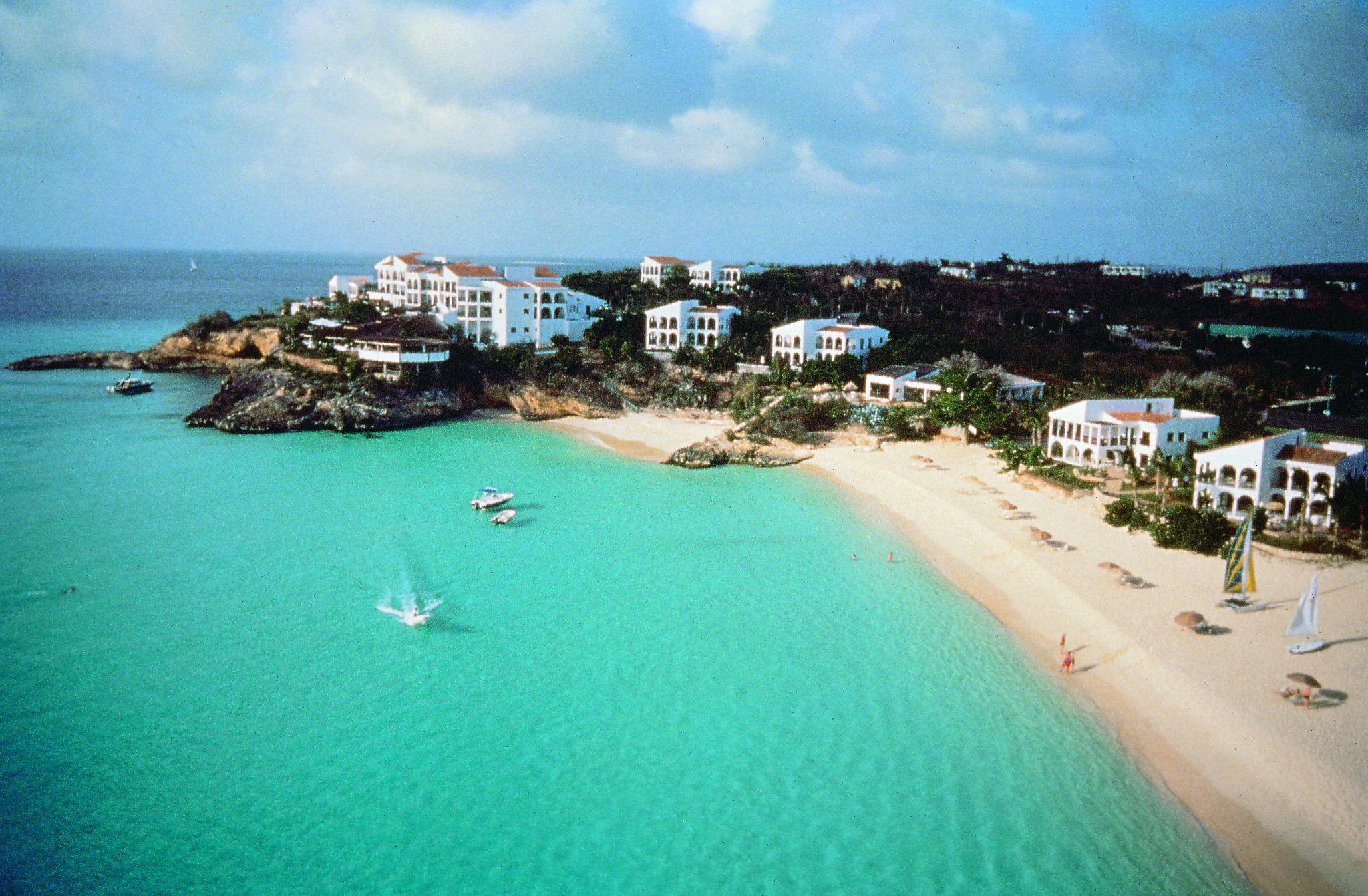 Malliouhana birds eye view of beach showing sand and ocean with boats in the sea and buildings around the outskirts of the sand