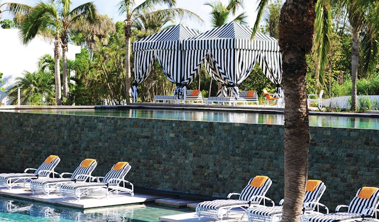 Malliouhana poolside lounge area with sunbeds shown around the pool and palm trees in the distance